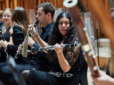 Students on stage holding wind instruments as part of the orchestra